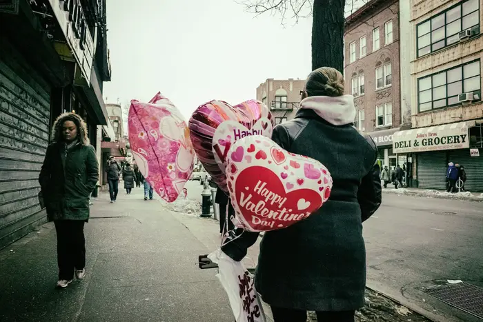 a photo of a woman walking in Brooklyn with valentine's day balloons